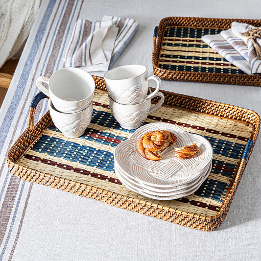 Woven tray with white ceramic dishes and cups on a light gray tablecloth.