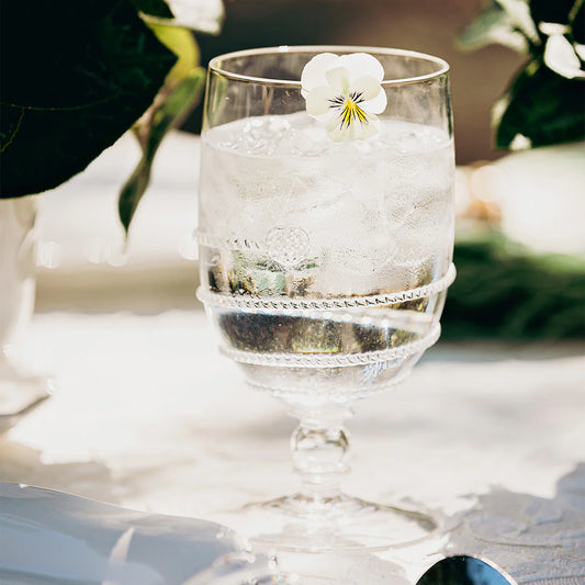 Clear glass with swirl motif and a floral garnish on a white surface with blurred greenery in the background
