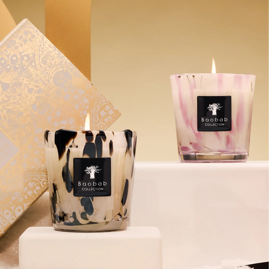 Two candles with decorative glass on a white surface with a gold archway in the background.