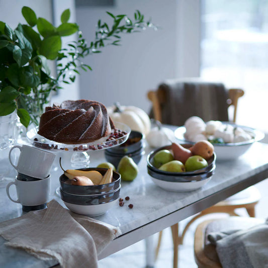 Dessert table with a bundt cake, fruit, and coffee cups in a cozy room.