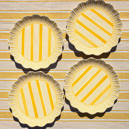 Four yellow scalloped and striped melamine plates on a tablecloth of the same color and pattern