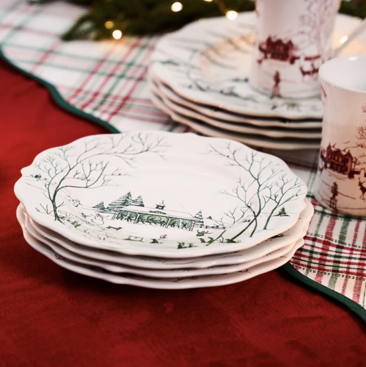 Stack of decorative green and white plates with a winter scene design on a red tablecloth.