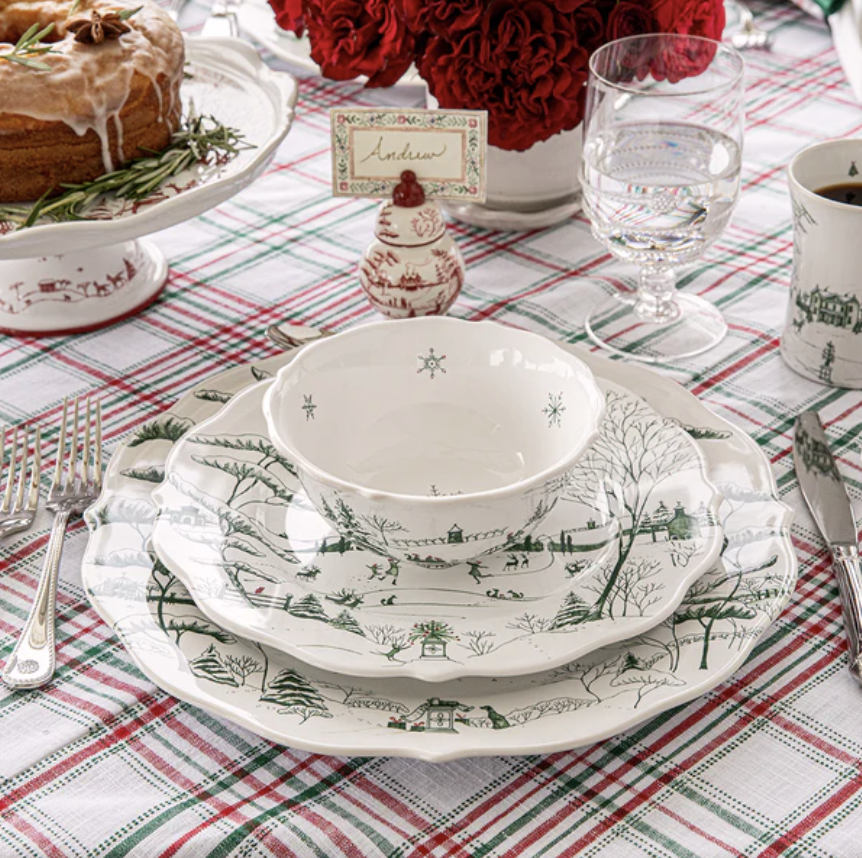 Christmas-themed table setting with green and white toile dishes, red and green plaid tablecloth, and decorative elements.