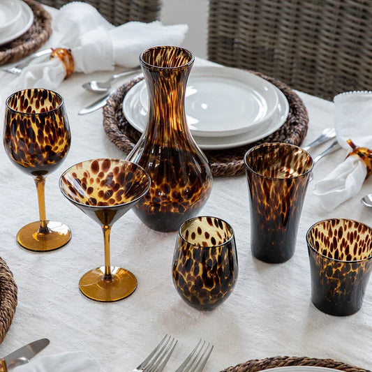 Table setting with brown tortoise-print glassware and a carafe on a white tablecloth.