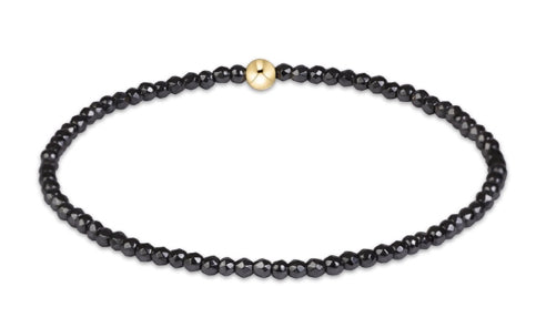 A beaded stretch bracelet made of small faceted black beads with a single round gold accent bead at the top center.