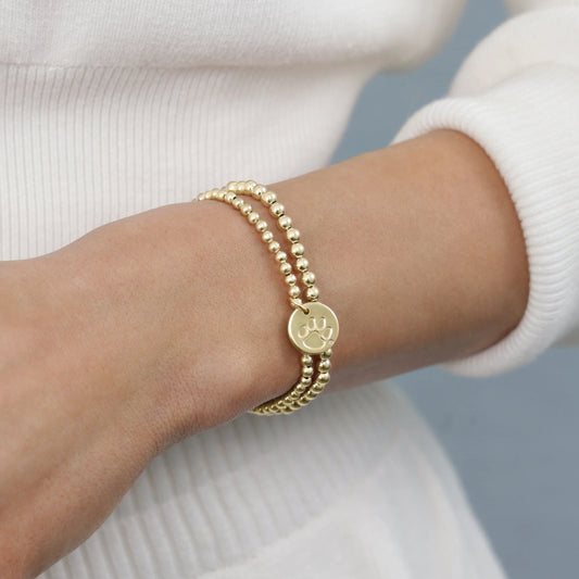 Gold bracelet with a paw print charm on a wrist against a neutral background