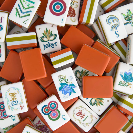 Decorative Mahjong tiles with a white tile face, with an olive green and powder blue stripe around the sides, and burnt orange-brown bottom to each tile. The tiles are in a random pile with different sides of each tile showing.
