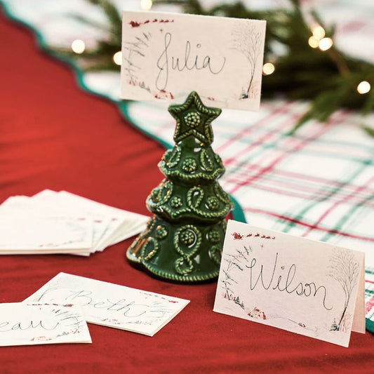 Green ceramic tree-shaped place card holder with green toile name cards on a festive tablecloth.