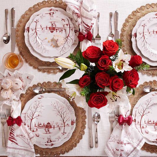 A table set for four with red and white toile holiday dishes and serveware and a red rose centerpiece
