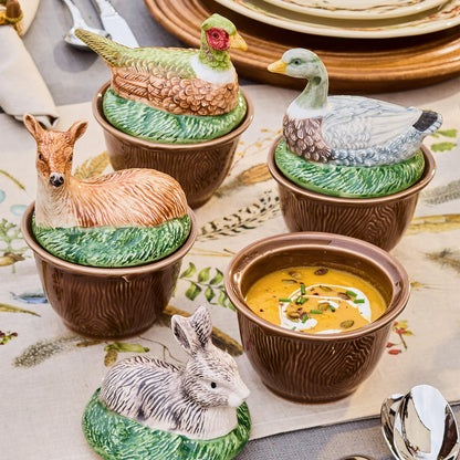 Ceramic animal-shaped bowls on a feathered tablecloth with a bowl of soup.