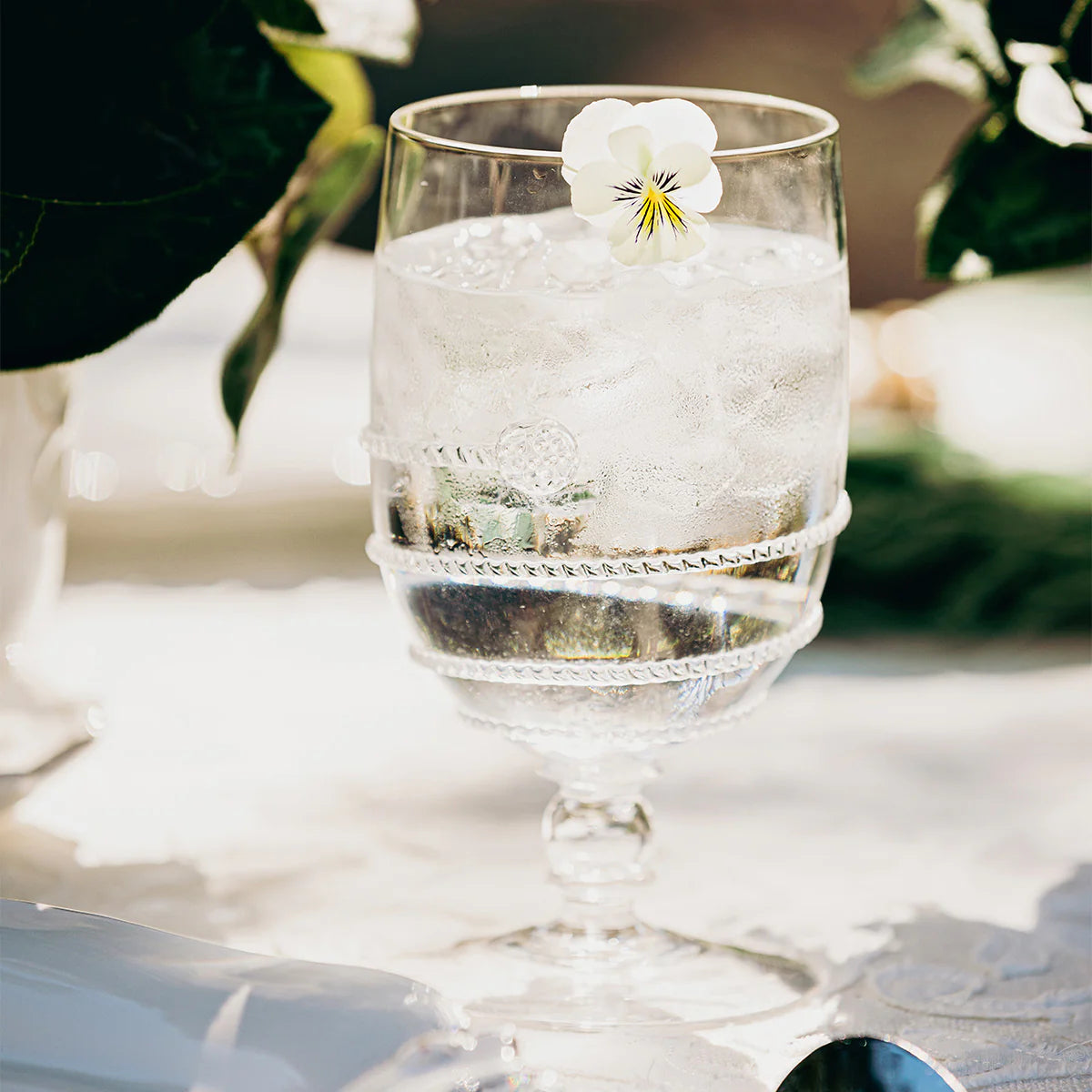 Clear glass with swirl motif and a floral garnish on a white surface with blurred greenery in the background