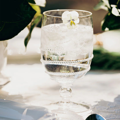 Clear glass with swirl motif and a floral garnish on a white surface with blurred greenery in the background