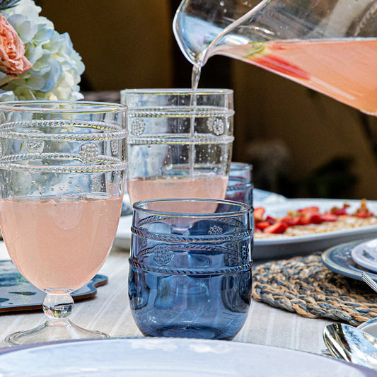 Pink lemonade being poured into small blue tumblers on an outdoor table with food and flowers
