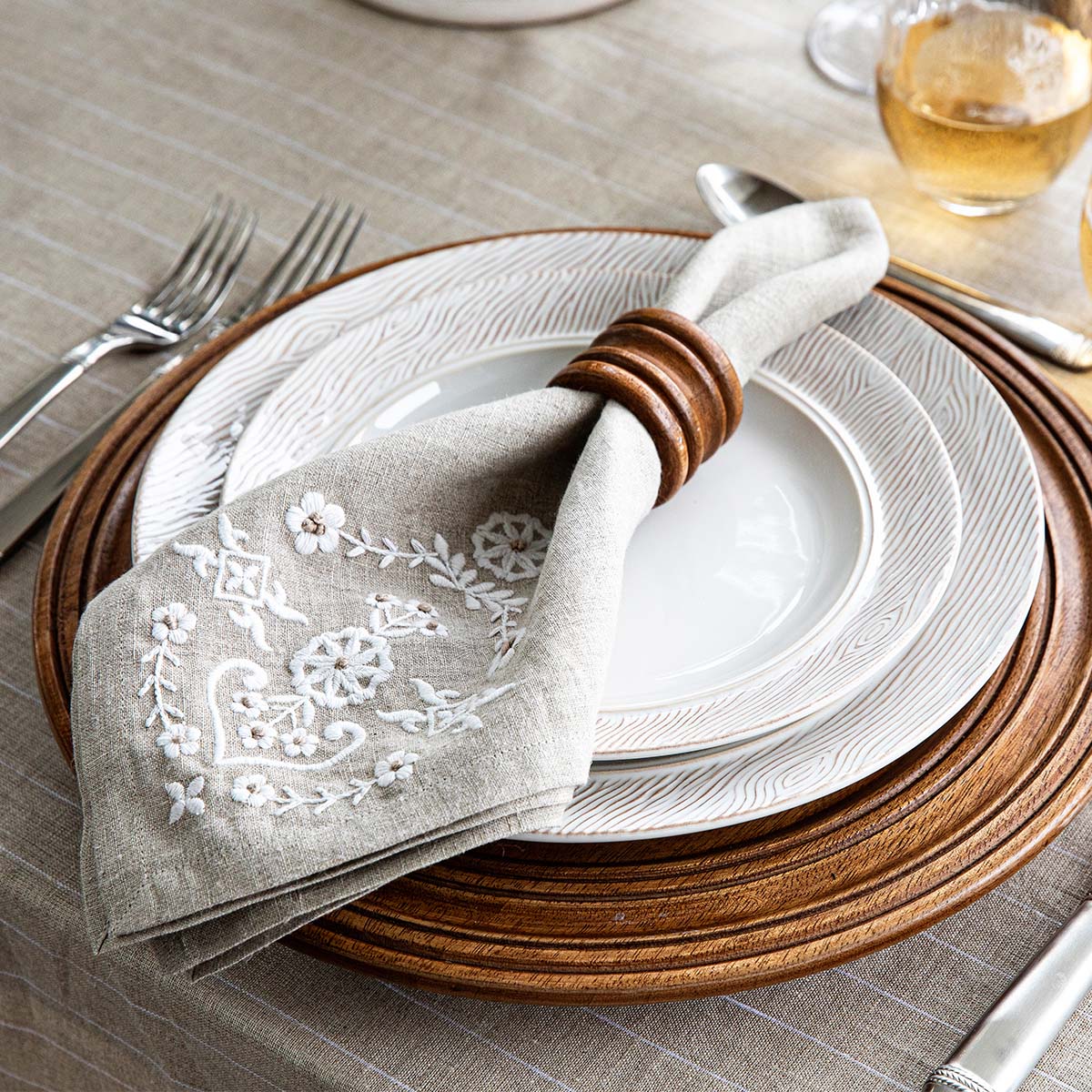 Elegant table setting with embroidered napkin, wooden charger, and white faux bois plates.
