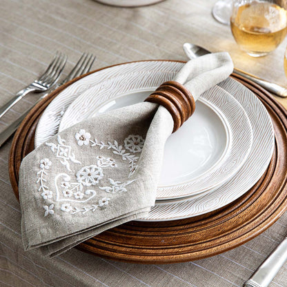 Elegant table setting with embroidered napkin, wooden charger, and white faux bois plates.