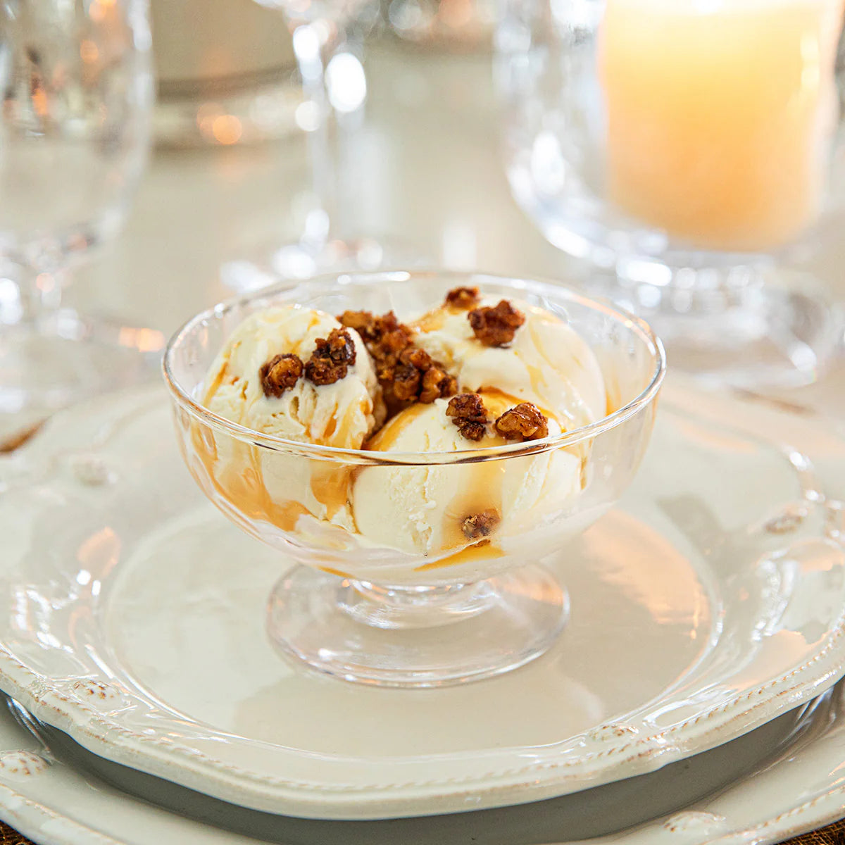 Glass bowl of ice cream with caramel and nuts on a white plate