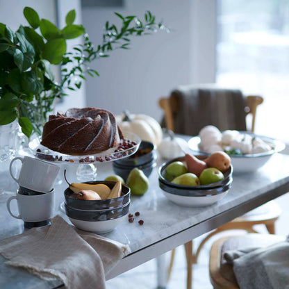 Dessert table with a bundt cake, fruit, and coffee cups in a cozy room. 