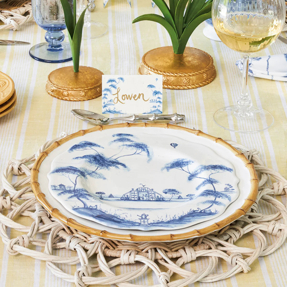 Decorative table setting with blue and white patterned salad plate, bamboo-rimmed dinner plate, and yellow striped tablecloth.
