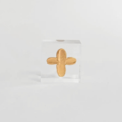Gold cross-shaped object on a clear stand against a white background