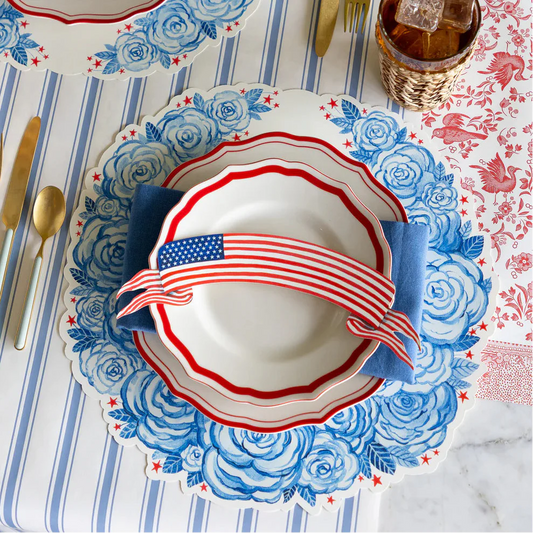 Decorative table setting with floral placemat, white plate with red and blue ribbon, and American flag design.