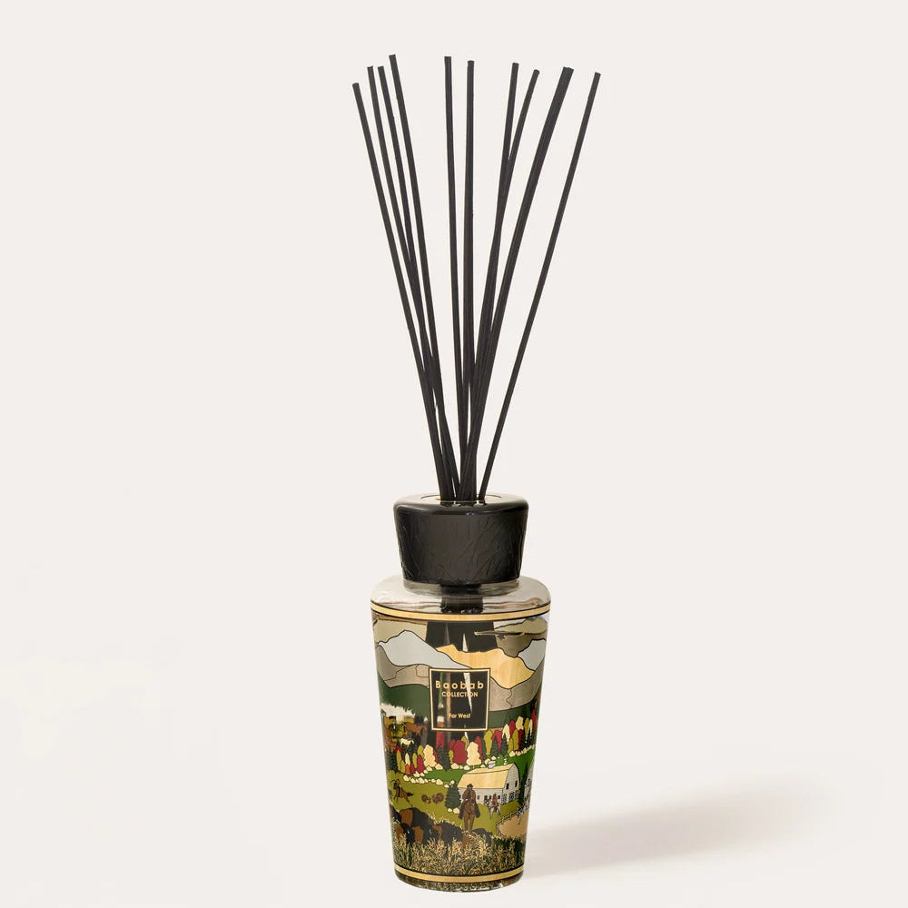 A reed diffuser bottle with a detailed landscape illustration on the glass, topped with a black cap and featuring black reeds.