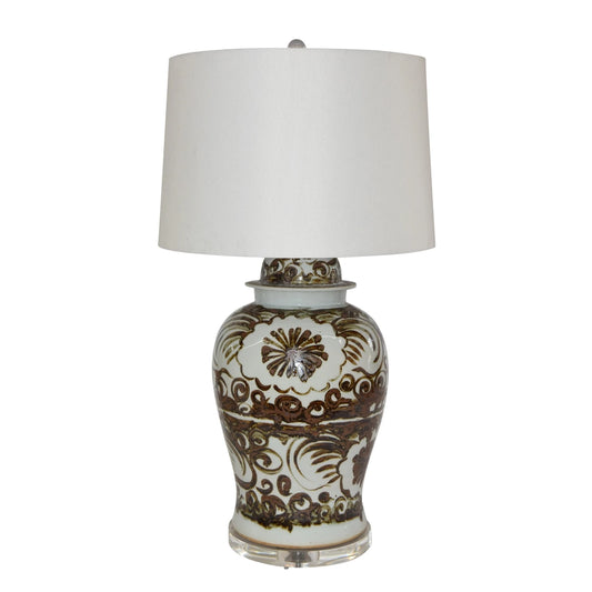 A table lamp with a white drum shade and a glossy white ceramic base decorated with brown floral and scroll patterns.