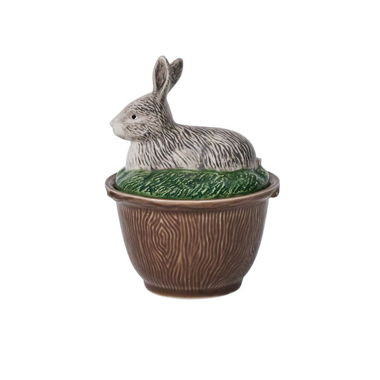 A brown-ceramic, faux bois bowl with a lid with a rabbit laying in grass.