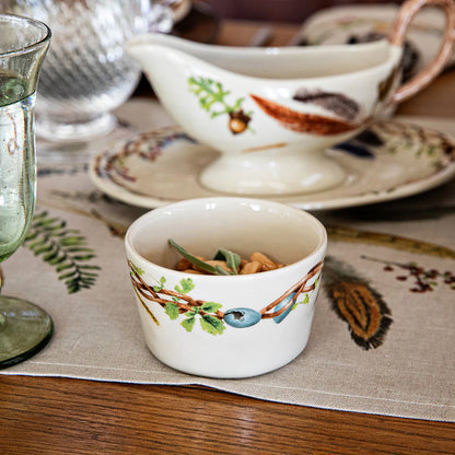 Decorative ceramic rameklin with nature-themed design on a table setting of other dishes in the pattern