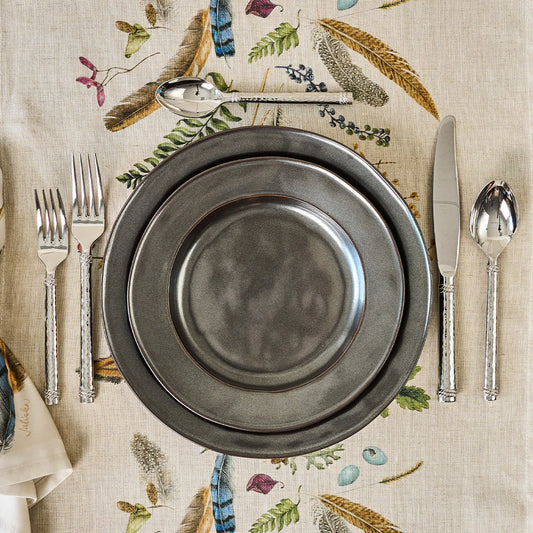Set table with hammered silverware and pewter plates on a feathered decorative tablecloth.