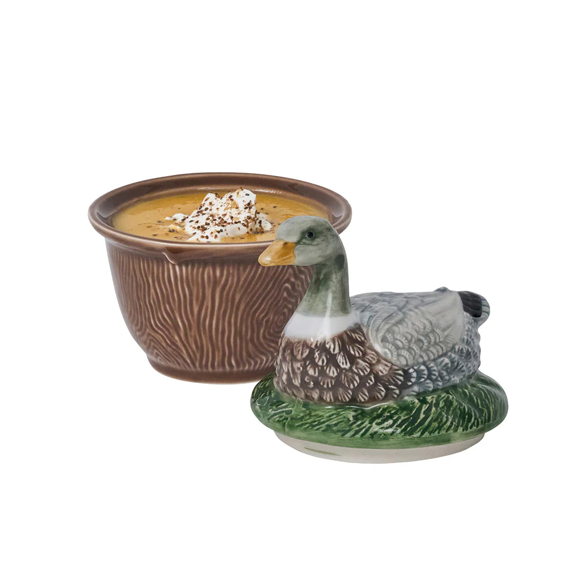 A brown-ceramic, faux bois bowl with soup positioned next to a lid with a duck laying in grass.