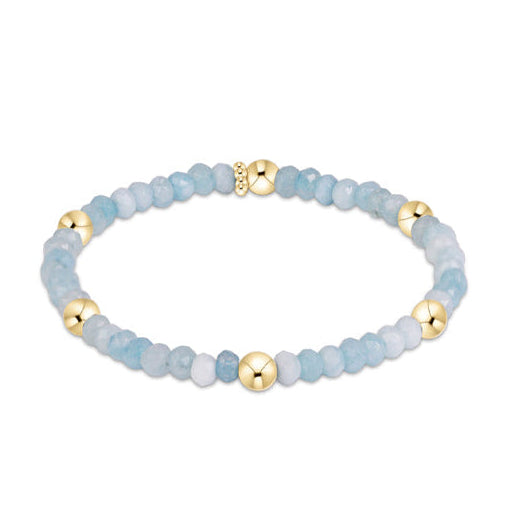 A beaded stretch bracelet featuring light blue and white marbled beads with polished gold spacer beads.