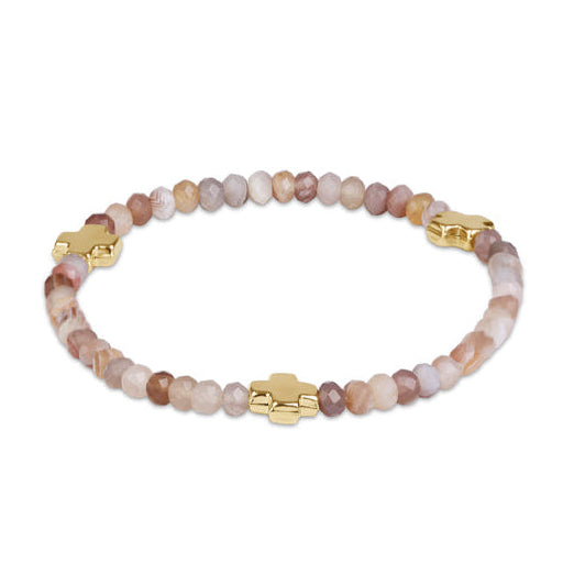A beaded stretch bracelet featuring faceted stone beads in shades beige accented by three gold-plated cross charms.