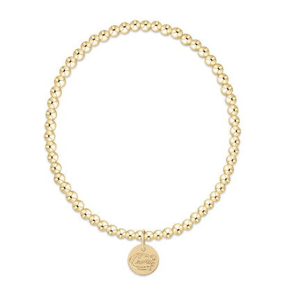 Gold beaded bracelet with a round disc charm on a white background
