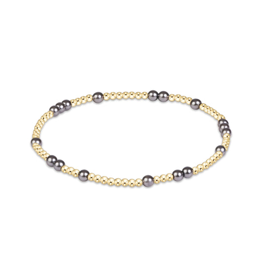 A beaded stretch bracelet featuring alternating strands of small gold-toned beads and larger dark gray pearls, displayed on a clean white background.