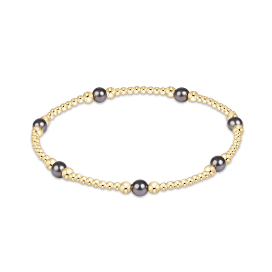 A beaded stretch bracelet featuring small gold-toned beads interspersed with larger dark gray freshwater pearls, shown on a clean white background.