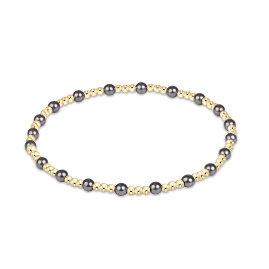 A beaded stretch bracelet featuring alternating dark gray pearls and small metallic gold beads, arranged in a circular shape on a solid white background.
