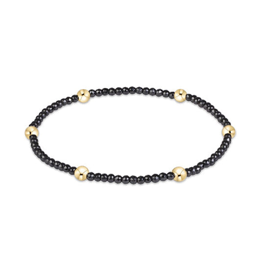 A beaded stretch bracelet featuring small black round beads separated by larger polished gold-tone round beads, shown on a plain white background.