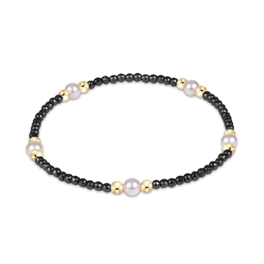 A beaded stretch bracelet featuring small black beads, larger white pearls, and polished gold spacer beads.
