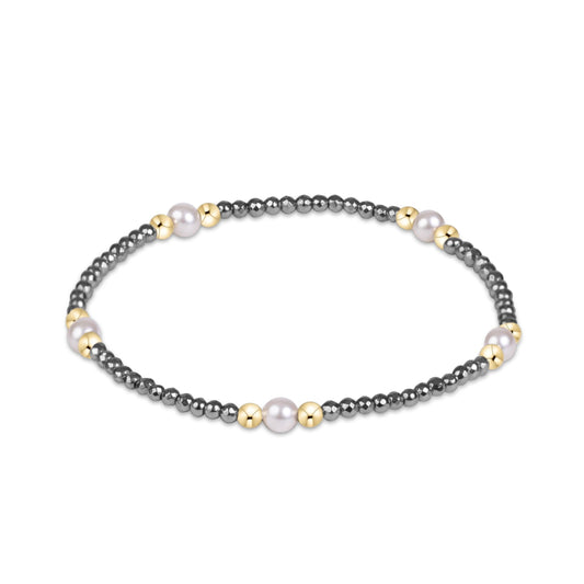 A beaded stretch bracelet featuring dark gray metallic beads, small gold spacer beads, and three larger white pearl-like beads.