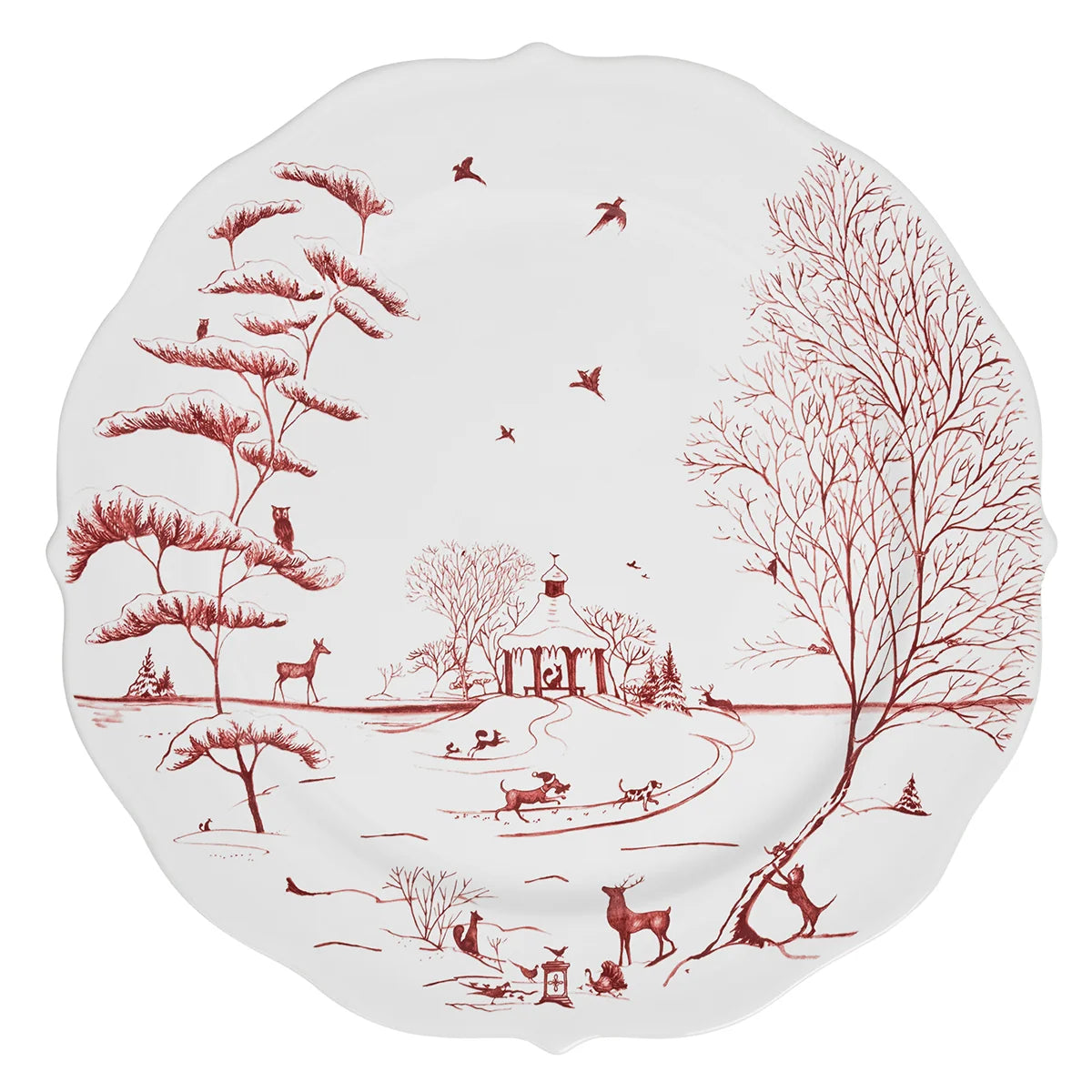 A scalloped white ceramic plate featuring a red winter landscape illustration with trees, birds, deer, and a small pavilion.
