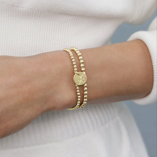 Gold bracelet with a circular charm on a wrist against a neutral background