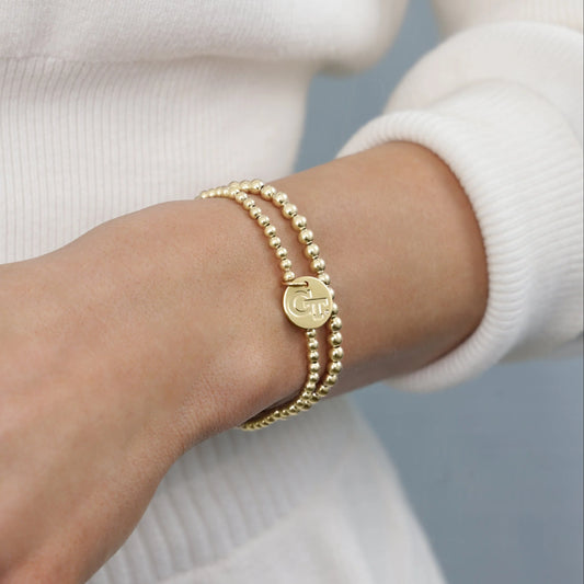 Gold bracelet with a logo on a wrist against a neutral background