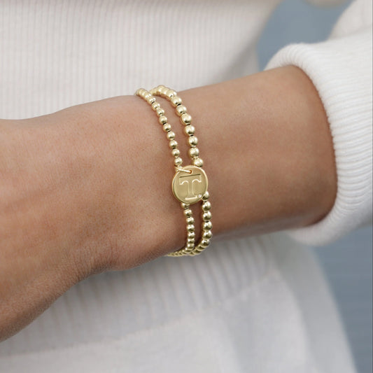 Gold bracelet with a circular charm on a wrist against a neutral background