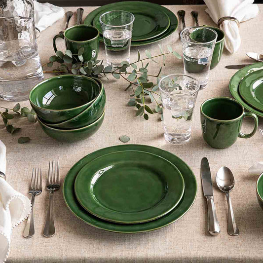 Green ceramic tableware set on a beige tablecloth with cutlery and glasses.