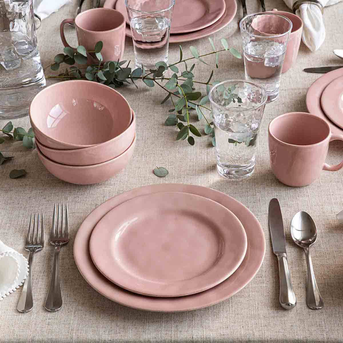 Pink ceramic tableware set on a beige tablecloth with greenery