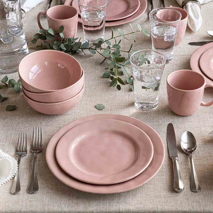 Pink ceramic tableware set on a beige tablecloth with greenery