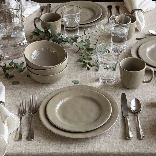 Elegant table setting with beige plates, cups, and silverware on a textured tablecloth.
