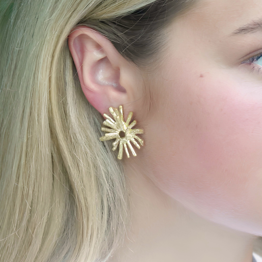 Close-up of a person wearing a gold sunburst earring.