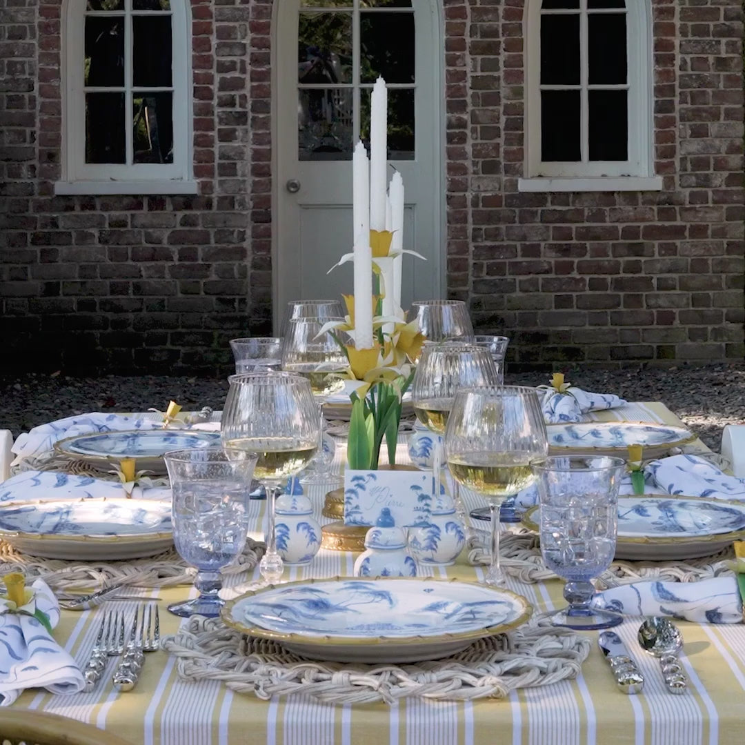 A video of an intricate table set with bamboo and blue toile dishes and decorate with yellow linens and centerpieces for a maximalist, happy look